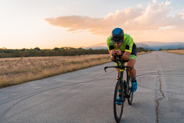Naklejka na ściany i meble Triathlete riding his bicycle during sunset, preparing for a marathon. The warm colors of the sky provide a beautiful backdrop for his determined and focused effort.