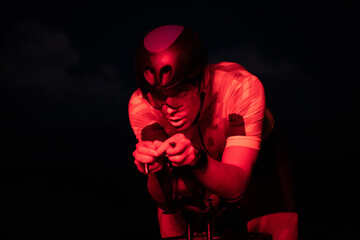 A triathlete rides his bike in the darkness of night, pushing himself to prepare for a marathon. The contrast between the darkness and the light of his bike creates a sense of drama and highlights the