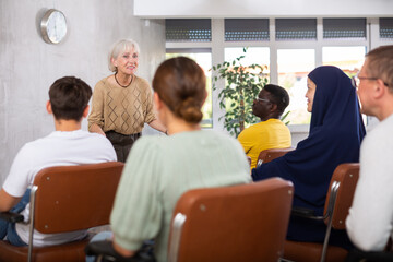 Emotional aged female tutor leading educational class for group of men and women of different nationalities sitting in auditorium