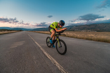 Fototapeta premium Triathlete riding his bicycle during sunset, preparing for a marathon. The warm colors of the sky provide a beautiful backdrop for his determined and focused effort.