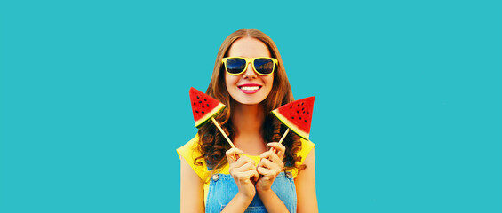 Fototapeta na wymiar Summer portrait of happy cheerful young woman with fresh juicy fruits, lollipop or ice cream shaped slice of watermelon on blue background