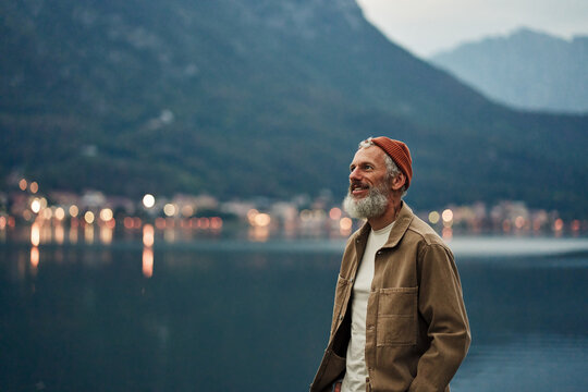 Happy Older Man Standing In Nature Park Enjoying Natural Park Landscape. Smiling Mature Active Traveler Exploring Camping Tourism Nature Lake And Mountains Travel Journey Feeling Freedom.