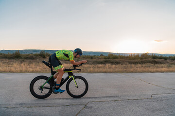  Triathlete riding his bicycle during sunset, preparing for a marathon. The warm colors of the sky provide a beautiful backdrop for his determined and focused effort.