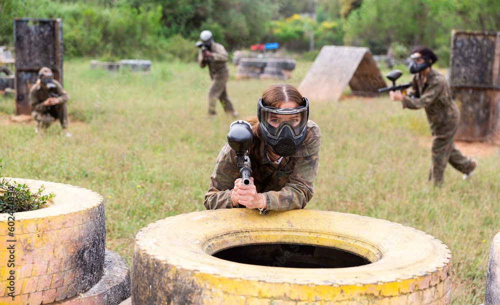 Wall mural Female paintball player in protective mask with ammunition and gun on paintball field