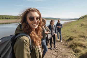 young adult woman by a river or lake with friends in the background, backpacker hiker backpack, light jackets and spring weather