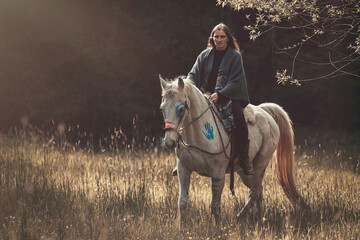 Portrait of a woman on her american native decorated white arabian horse in spring outdoors