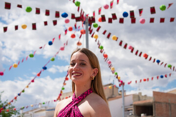 Blonde girl smiling. Happy young Caucasian woman dressed in a pink top, smiling joyfully, showing her happiness and well-being to someone. Body language. Young girl smiling at a festival. Party.