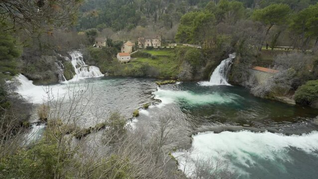 Waterfalls From Every Side Flow Into Green Pool With Buildings Above