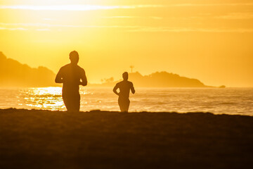 Fototapeta premium silhouette of people running at dawn on leblon beach in rio de janeiro.