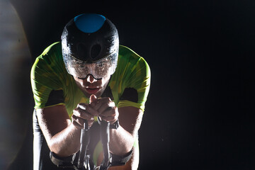 A triathlete rides his bike in the darkness of night, pushing himself to prepare for a marathon. The contrast between the darkness and the light of his bike creates a sense of drama and highlights the