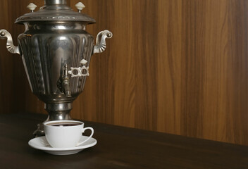 Vintage samovar and cup of hot drink served on wooden table, space for text. Traditional Russian...
