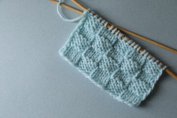 Soft turquoise knitting and needles on light blue background, top view. Space for text