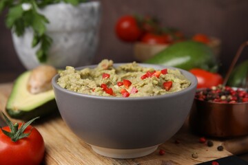 Bowl of delicious guacamole and ingredients on wooden board, closeup