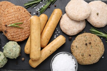 Different raw vegan meat products, salt and rosemary on dark board, flat lay