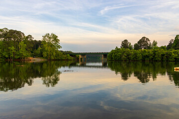 Fototapeta na wymiar a gorgeous spring landscape at Proctor Landing Park at sunset with rippling water surrounded by lush green trees and plants and bridge over the water at Lake Acworth in Acworth Georgia USA
