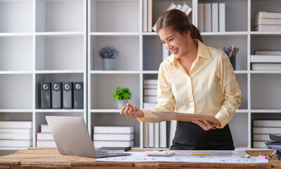 Young female manager reading email with good news on computer raising hand in yes gesture, celebrating at her desk.