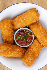 Top view of fried mozzarella cheese fingers with a red spicy dipping sauce, in a white bowl on the...