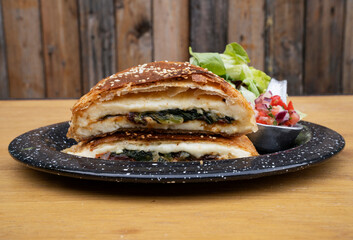 Gastronomy. Closeup view of a bun made with grilled provolone cheese, spinach, sun dried tomatoes and puff pastry, in a black rustic dish on the restaurant wooden table.
