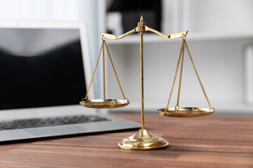 Symbolizing justice and legal authority, golden balanced scale on desk with laptop in law office...