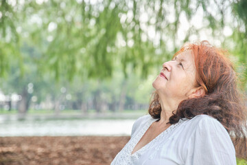 Portrait of a latin senior woman smiling looking up daydreaming in nature. Bright composition with copy space. Concept: peace of mind and happiness enjoying leisure time during retirement.