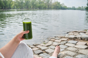 Unknown person holding a bottle of green juice outdoors. Concepts: wellness, nourishment, healthy...