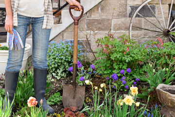 Woman standing in a garden holding garden gloves and spade