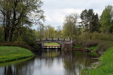 Fototapeta na wymiar View of the Slavyanka River and the Viscontiev Bridge in the Pavlovsk Palace and Park Complex on a sunny spring day, Pavlovsk, Saint Petersburg, Russia
