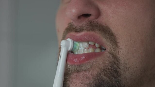 Close-up of man cleaning teeth by an ultrasonic toothbrush. Male brushing his teeth with electric teethbrush. Theme oral health and dental hygiene. Morning sanitation procedures in the bathroom. 