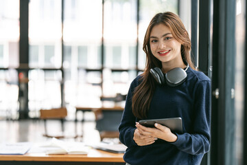 Obraz premium Young Beautiful university student with headphone holding tablet standing in co-workspace.