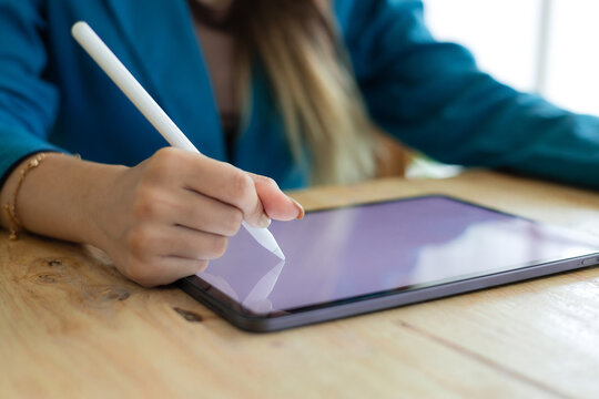 Close up image of a woman is using stylus pen and empty screen tablet at the wooden table.