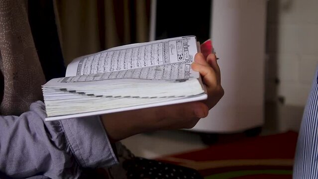The palms of a Muslim woman are holding an Islamic holy book, the Qur'an, open and being read. .