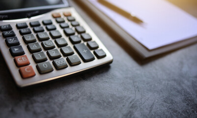 Close up shot of Calculator place beside the paper and pen on accounting desktop with orange light. Copy space on the bottom section.