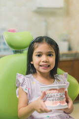 Asian girl in dental chair, with tooth brush. Medicine, dentistry and healthcare concept
