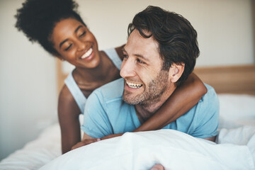 Fototapeta premium Happy couple, bed and hug laughing for morning, relax or bonding relationship at home. Interracial man and woman smiling, hugging and laugh in joyful happiness or relaxing weekend together in bedroom