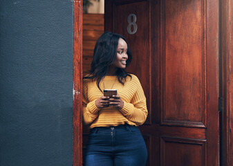 Doorway, woman and phone for social media, texting and happy while reading message in front of house. Smartphone, influencer and african female online for blog, networking or property app review