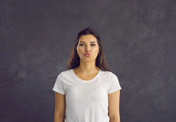 Portrait of beautiful young woman standing on gray background with folded lips in anticipation of kiss. Cheerful and flirtatious caucasian woman who is ready to take kiss. Concept of human feelings.