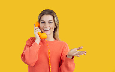 Portrait of smiling millennial girl isolated on yellow background look at camera talk on corded phone. Happy young woman have pleasant conversation or call on landline telephone. Communication. - obrazy, fototapety, plakaty