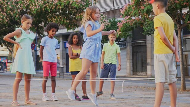 Multiracial group of cheerful preteen children having fun together outdoors on summer day, playing chinese jump rope on city street