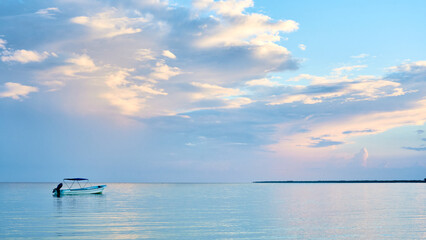 a fishing boat on the seashore of holbox, a beach in the riviera maya. a sky with many clouds painted in blue and pink. very relaxing landscape.