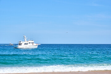 white yacht in the pacific ocean, waves at the shore and golden sand, baja california sur, los cabos, mexico.