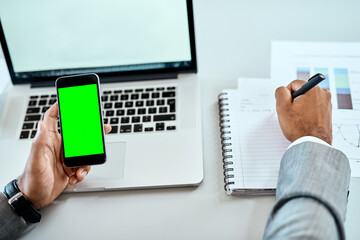 Phone, green screen and man hands writing notes, ideas and laptop planning for mobile app mockup and business website. Multimedia, computer and person with smartphone mock up, notebook and research