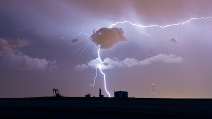 Vivid lighting over an oil well and antenna in an otherwise empty field.