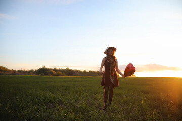 A girl in a hat on a walk in the park. A girl with a basket walks in the spring. A girl is walking along the road at sunset.