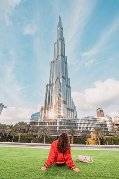 17 January 2023, Dubai, UAE: happy traveler girl sitting on a green lawn and enjoying incredible view of majestic Burj Khalifa tower in Dubai, UAE