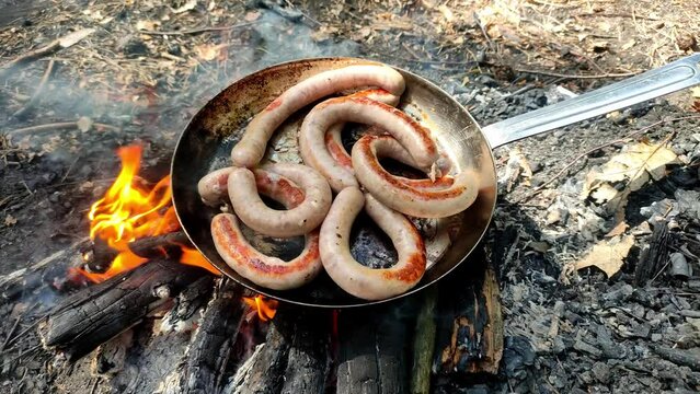 Sausages are fried in a pan on an open fire in the forest at a picnic
