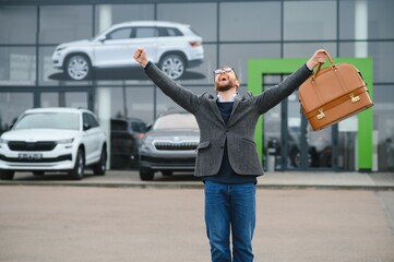 Happy buyer near the car in front of the modern avtosalon building