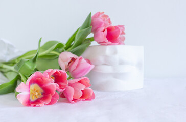 Fototapeta na wymiar Pink tulips bouquet and plaster statue of lips lying on white wrinkled blanket background copy space