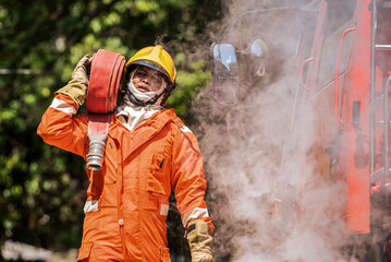Obraz premium The firefighter's determined gaze pierces through the haze as he navigates the chaotic scene carrying the fire hose with a show symbol of his commitment to extinguishing the flames.