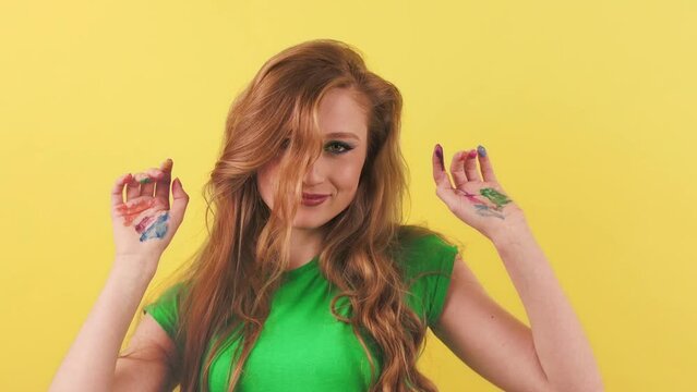 A beautiful young woman shows her palms painted in different colors. Cheerful red-haired girl dances in front of the camera with painted hands.
