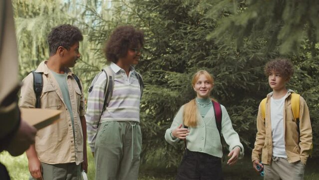 Medium shot of group of multiracial kids chatting during school one day trip to summer forest with ranger